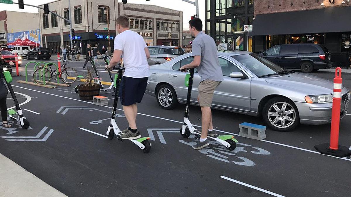 Scooter riders use the temporary “Better Block” lanes on Oak Street in the East Crossroads.