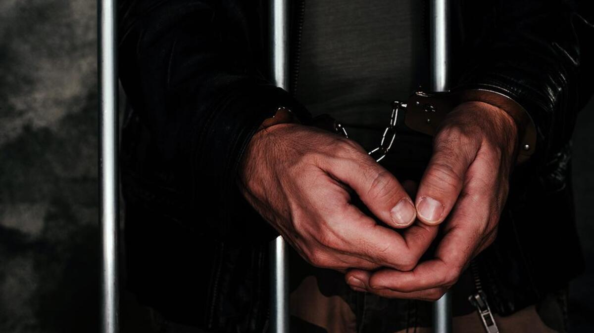 Handcuffed man behind prison bars. Arrested criminal male person imprisoned.