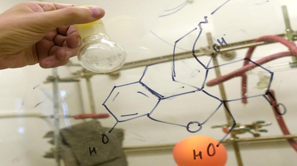 Andrew Coop, Ph.D, associate dean of academic affairs and pharmacy professor at the University of Maryland School of Pharmacy, holds a container with dosages of a new kind of opioid, one that he says doesn't cause dependence. Drawn on the glass is the chemical structure for UMB24, the new kind of opioid.
