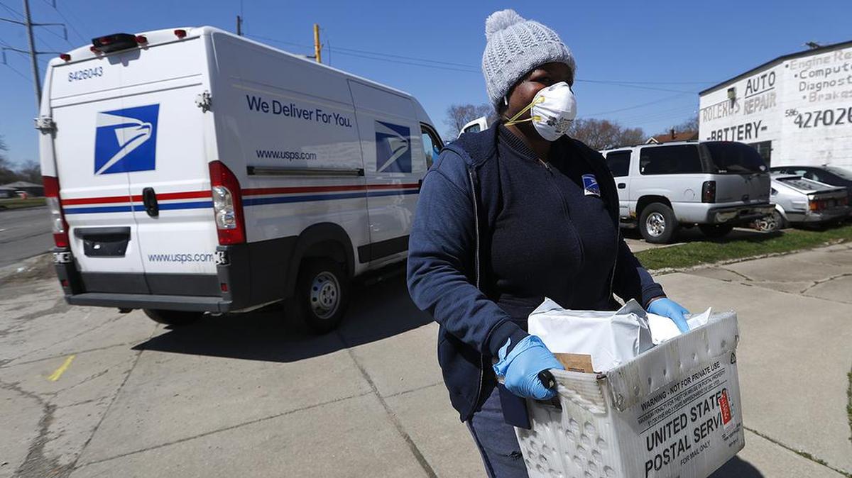 A United States Postal worker makes a delivery with gloves and a mask in Warren, Mich., Thursday, April 2, 2020. The U.S. Postal Service is keeping post offices open but ensuring customers stay at least 6 feet (2 meters) apart. The agency said it is following guidance from public health experts, although there is no indication that the new coronavirus COVID-19 is being spread through the mail. (AP Photo/Paul Sancya)