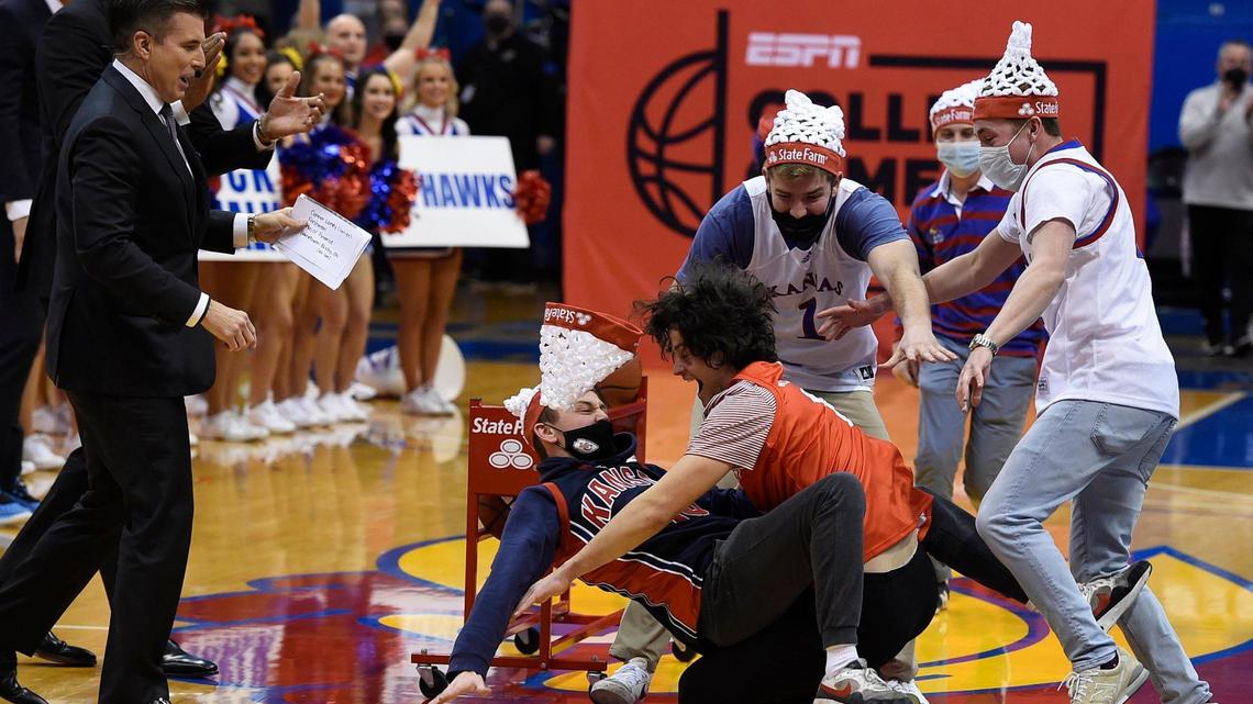 After hitting a half-court shot that earned him $19,000, University of Kansas student Connor Loney, wearing red, of Bixby, Oklahoma is mobbed by his friends as ESPN’s College GameDay hosts Rece Davis and LaPhonso Ellis, left, look on Saturday morning at Allen Fieldhouse in Lawrence.