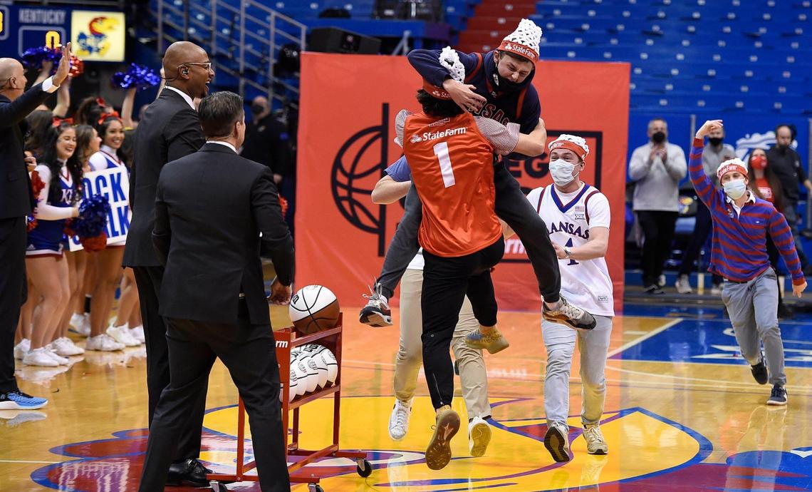 After hitting a half-court shot that earned him $19,000, Connor Loney, wearing red, of Bixby, Oklahoma is mobbed by his friends as ESPN’s College GameDay hosts Rece Davis and LaPhonso Ellis, left, look Saturday morning at Allen Fieldhouse.
