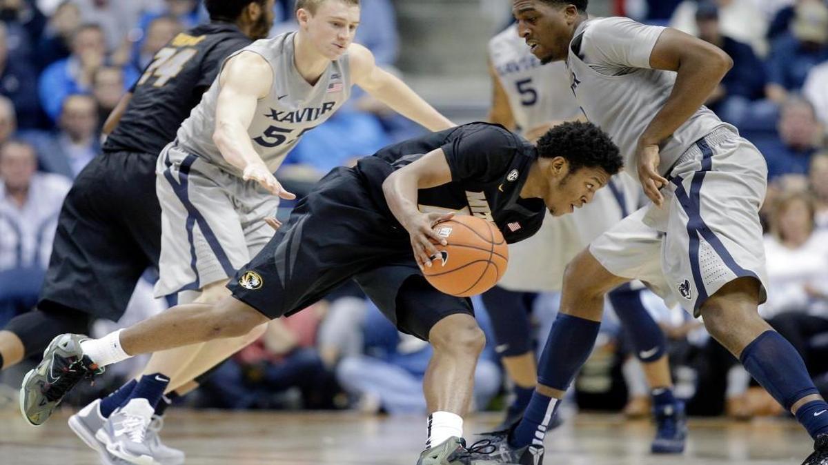 Missouri’s Namon Wright (12) drove past Xavier’s J.P. Macura (55) and James Farr (right) in the first half Tuesday night in Cincinnati. The Musketeers beat the Tigers 78-66, Missouri’s first loss in three games this season.