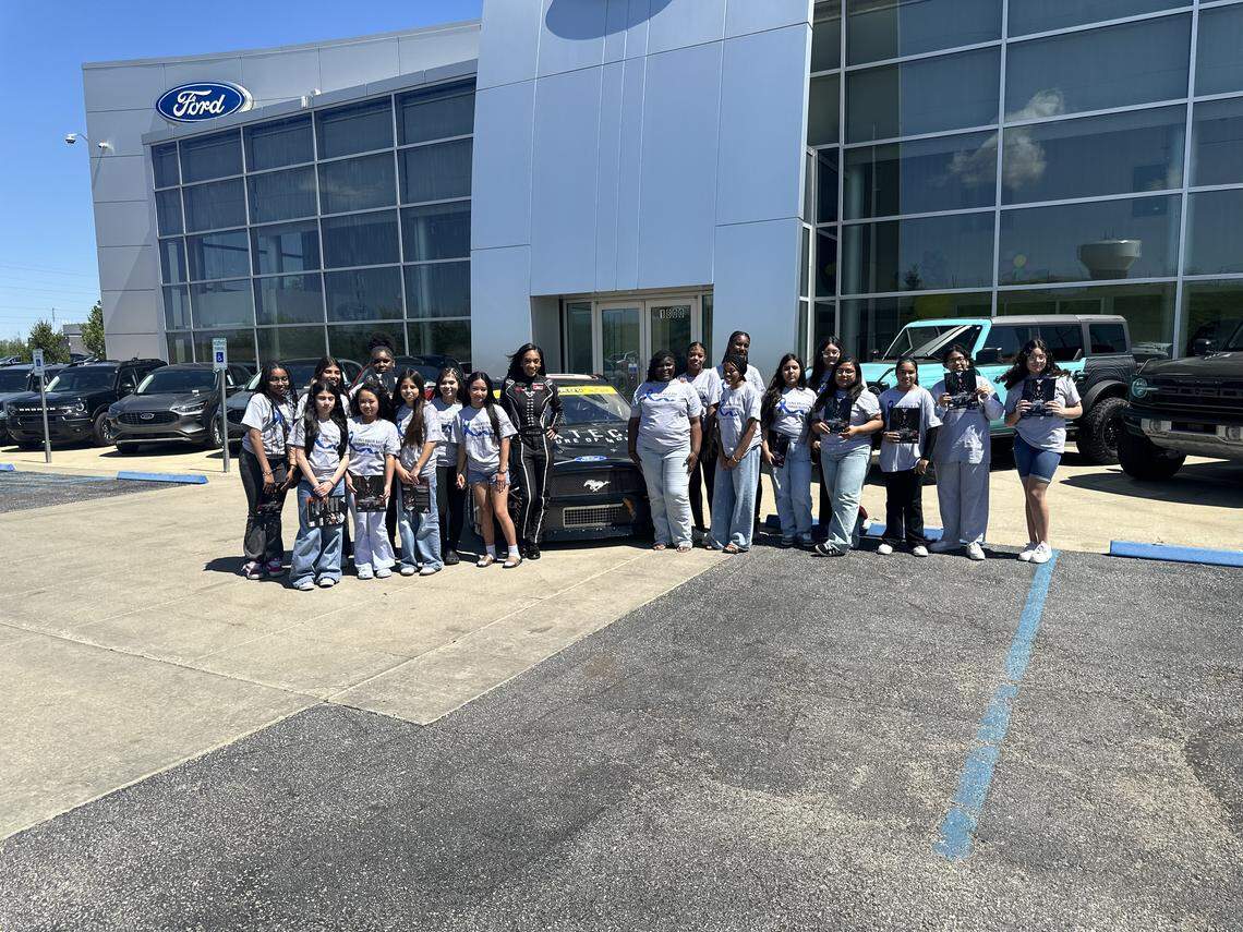 Stock car driver Dystany Spurlock takes a picture with Gloria Willis Middle School students in front of her No. 66 Ford Mustang at Victory Ford in Kansas City, Kansas.