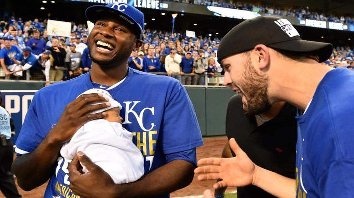
Royals center fielder Lorenzo Cain held his son, Cameron Loe Cain, while he and third baseman Mike Moustakas celebrated after the Royals beat the Baltimore Orioles 2-1, winning the ALCS.
