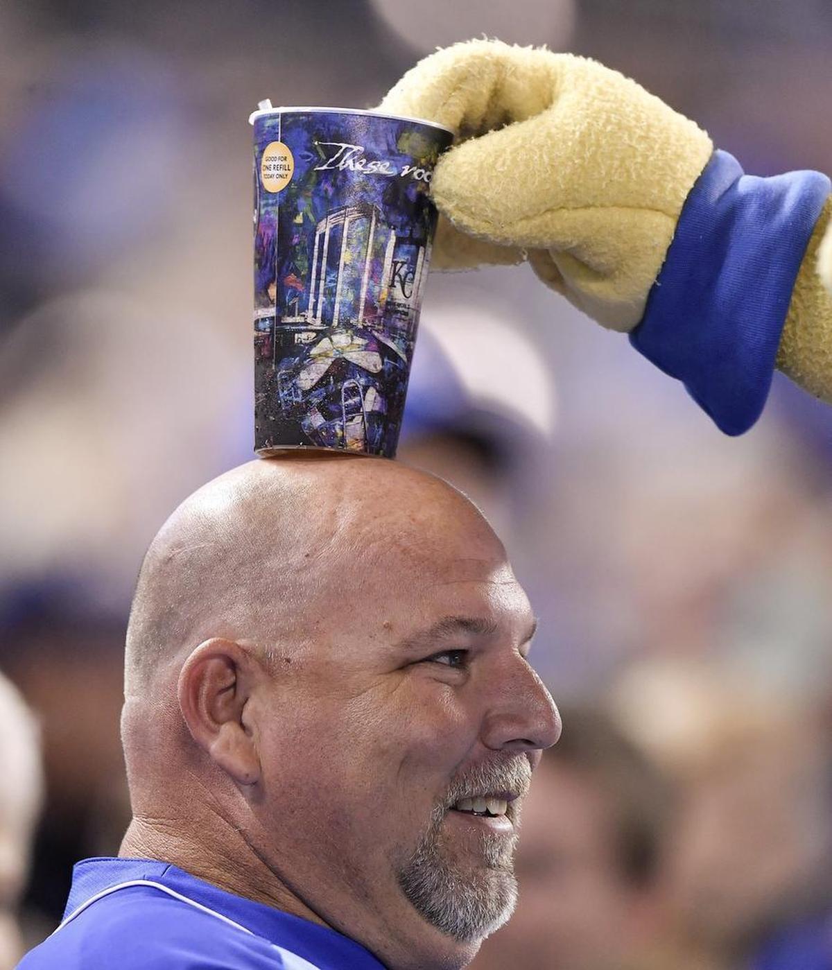 Kansas City Royals mascot Sluggerrr balances a drink on a fan’s head during a 2017 game against the Detroit Tigers at Kauffman Stadium.