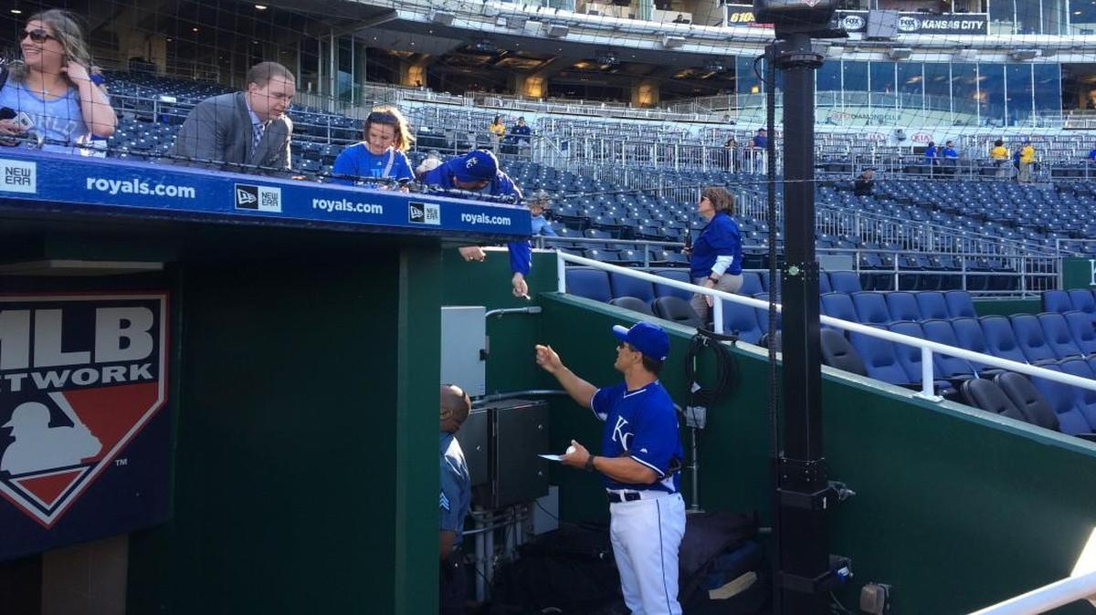 Royals bench coach Don Wakamatsu signs autographs for fans Sunday evening through an access area in Kauffman Stadium’s expanded safety netting.