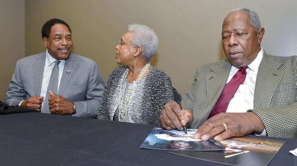 Hank Aaron (right) signed autographs as his wife Billye Aaron talks with former baseball player Dave Winfield on Saturday at the Negro Leagues Baseball Museum’s 25th anniversary gala.