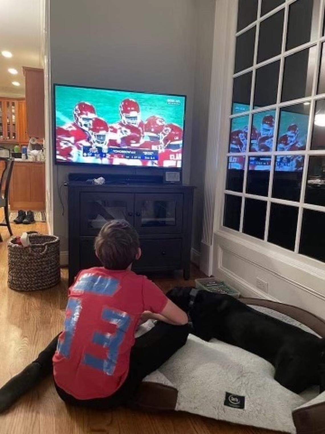 Kevin Jee watches a Kansas City Chiefs 2022 playoff game against the Buffalo Bills on television at his home in Cary, North Carolina, while wearing a handmade No. 83 Noah Gray jersey he constructed out of both blue painter’s and scotch tape.