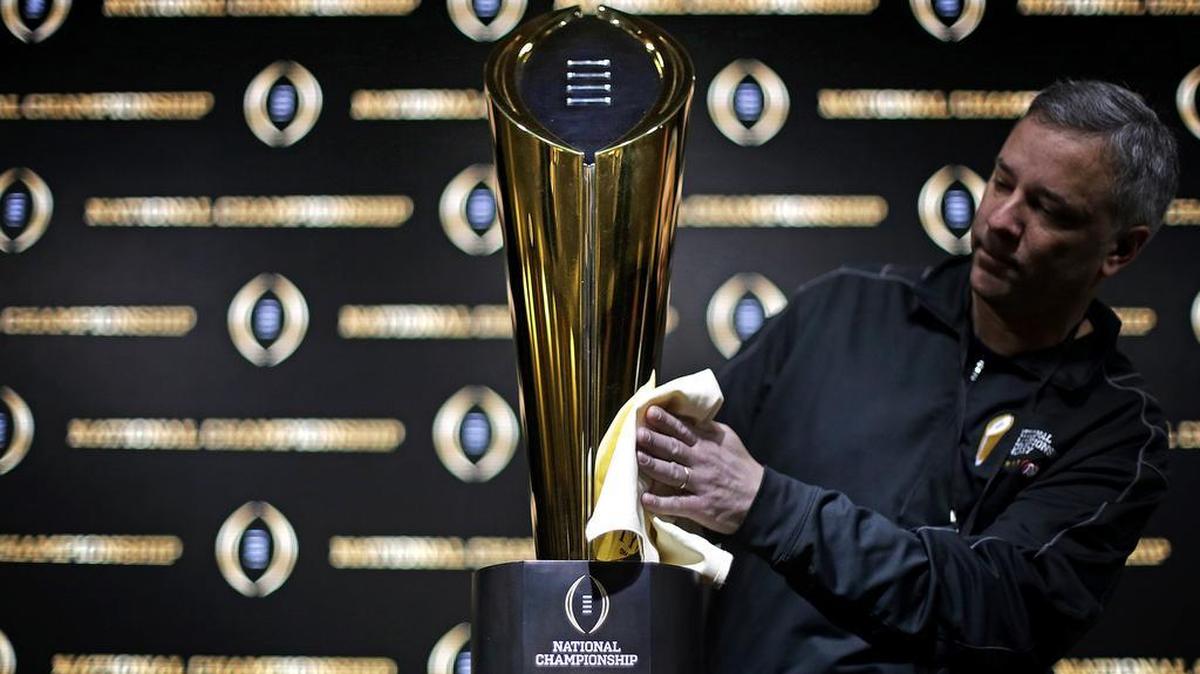 Charley Green buffs the NCAA college football championship trophy before a coaches news conference in Atlanta on Sunday. Georgia and Alabama will play for the NCAA football national championship on Monday.