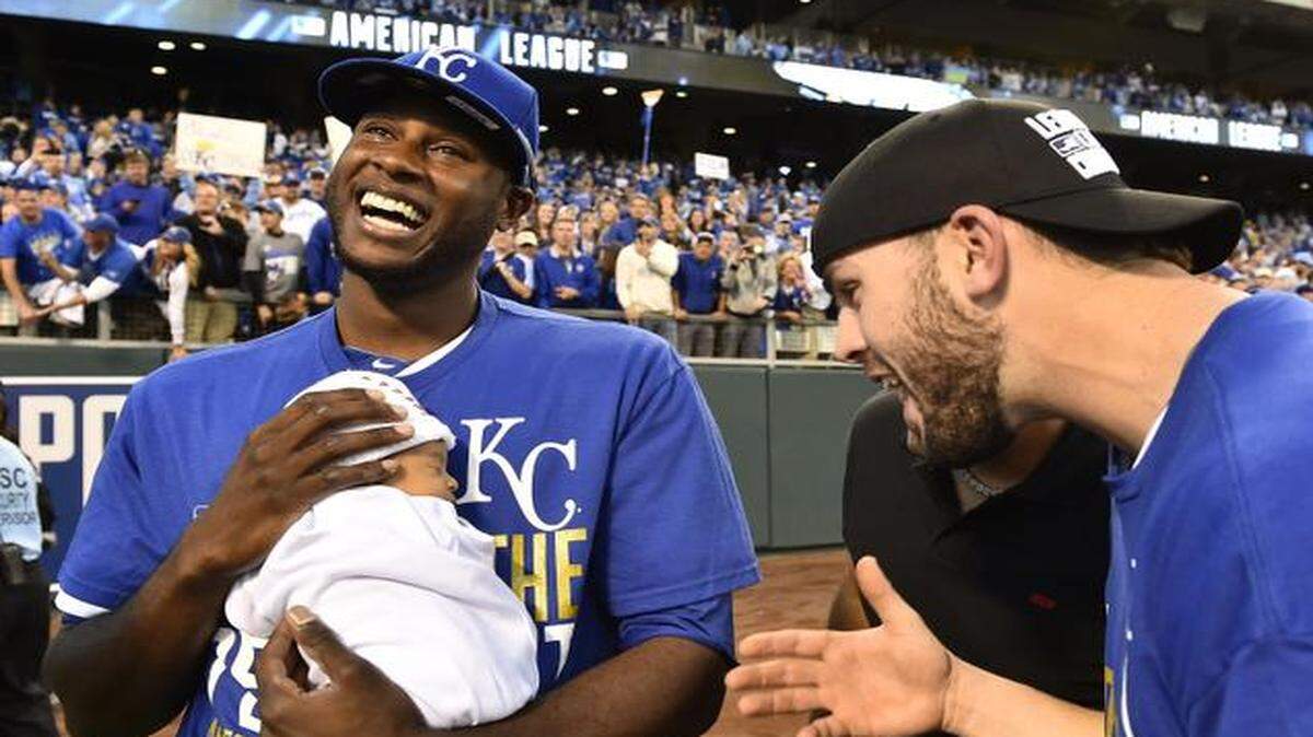 
Kansas City Royals center fielder Lorenzo Cain held his infant son, Cameron Loe Cain, as teammate Mike Moustakas celebrated after a series-clinching 2-1 win against the Baltimore Orioles in game four of the American League Championship Series.

