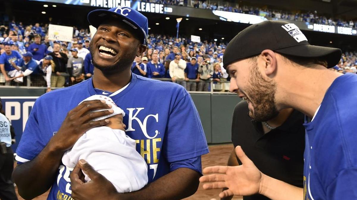 Kansas City Royals center fielder Lorenzo Cain held his young son Cameron Loe Cain as teammate Mike Moustakas celebrated after the Royals won the American League pennant in 2014.