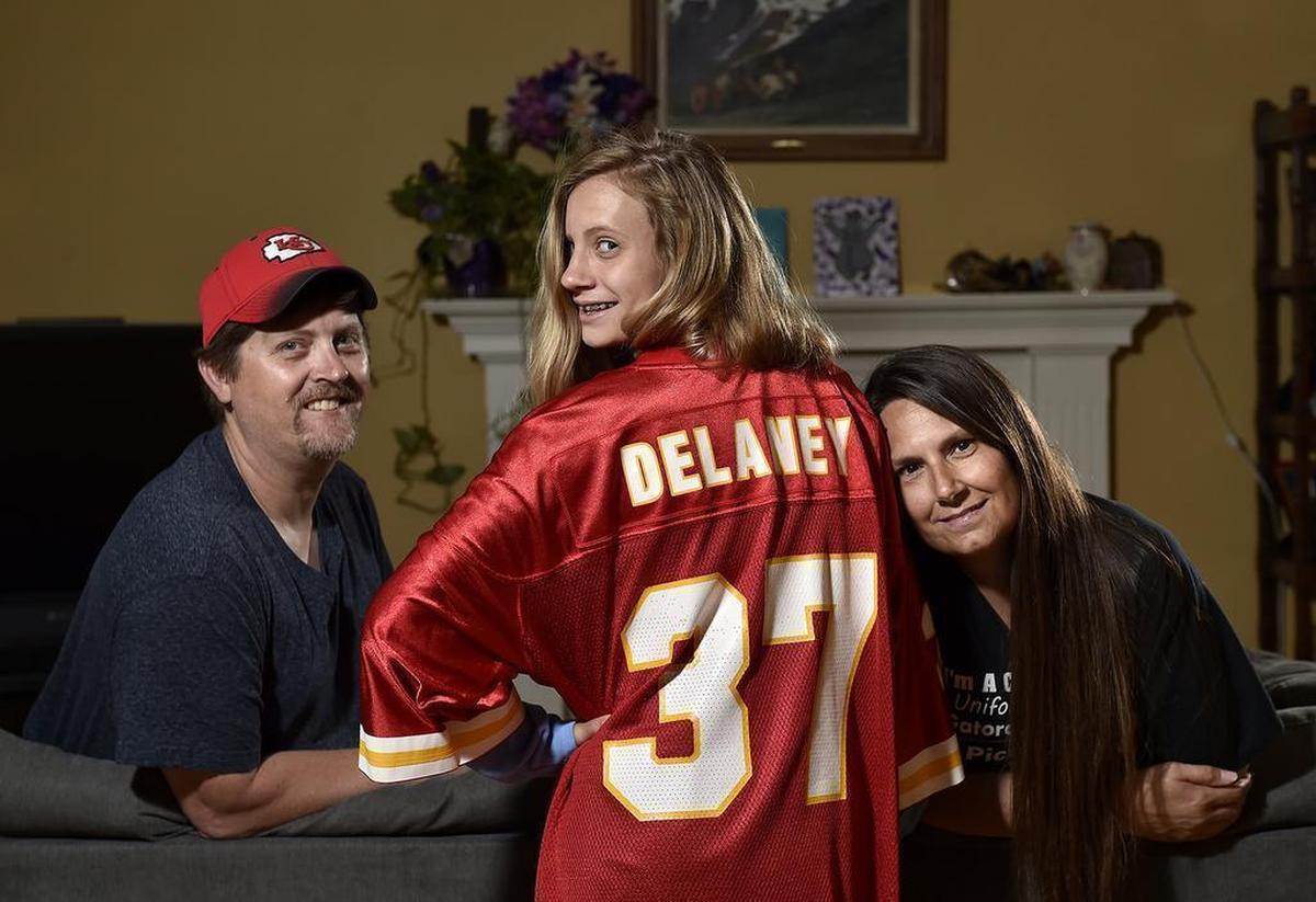 Mark (left) and Kelly Neath named their daughter after Joe Delaney, a running back for the Chiefs who drowned trying to save three children in Louisiana in 1983. Delaney, now 15, in their Shawnee home with her dad and mom, wears Mark’s No. 37 Chiefs jersey.